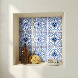 May include: A built-in bathroom shelf with blue and white patterned tiles. The shelf contains a brown soap dispenser, a natural sponge, and a white soap dish with a bar of soap. The tiles have a floral design.