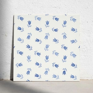 Puede incluir: Un azulejo cuadrado con un patrón repetitivo de pequeñas flores azules pintadas a mano, similares a tulipanes, sobre un fondo blanco roto. Los motivos florales están dispuestos en una cuadrícula, cada uno con un tallo y dos hojas.