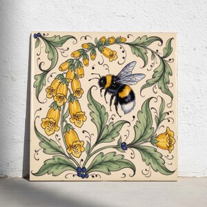 Könnte beinhalten: Eine quadratische Keramikfliese mit einer handgemalten Illustration einer Hummel im Flug, umgeben von gelben glockenförmigen Blüten und grünem Blattwerk. Das Design ist auf einem cremefarbenen Hintergrund mit verschlungenen Ranken.