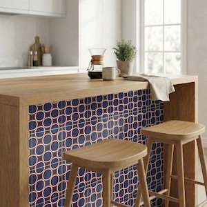 Puede incluir: Isla de cocina con encimera de madera y salpicadero de azulejos azul marino con un patrón repetido de círculos rojos y blancos. Dos taburetes de madera frente a la isla. Una cafetera, una taza y una planta están en la encimera.