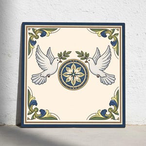 Könnte beinhalten: Quadratische dekorative Fliese mit zwei weißen Tauben, die Olivenzweige tragen, und einem zentralen Blumendesign. Die Fliese hat einen cremefarbenen Hintergrund, einen marineblauen Rand und dekorative Eckelemente in Grün und Blau. Ca. 30 cm x 30 cm.