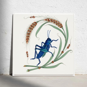 May include: A square white ceramic tile featuring a detailed illustration of a vibrant blue grasshopper positioned centrally. The insect is surrounded by curved stalks of wheat with golden-brown grains and long, slender green leaves.