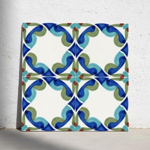 Puede incluir: Un azulejo de cerámica cuadrado con un patrón repetitivo de formas curvas en azul, azul claro y verde salvia sobre un fondo blanco. El diseño incluye pequeños puntos rojos en las intersecciones de los motivos florales, creando una disposición simétrica.