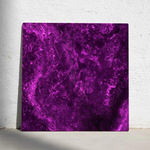 May include: A square canvas with a vibrant, abstract design in shades of purple. The artwork features a marbled effect with swirling patterns and dark veins, creating a textured appearance. The canvas is leaning against a white wall.