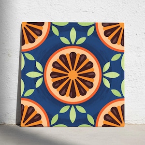Puede incluir: Arte en lienzo cuadrado con un patrón repetido de rodajas de naranja y hojas verdes sobre un fondo azul oscuro. Las rodajas de naranja tienen detalles marrones y naranjas. La obra de arte se exhibe contra una pared blanca.