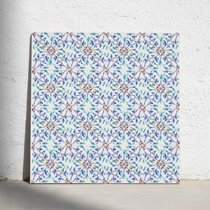 May include: A square decorative tile featuring a repeating symmetrical pattern of blue and turquoise floral vines on a white background, accented with small red circular motifs at the center of each intersection of the intricate botanical design.