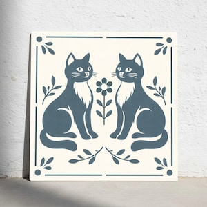 Puede incluir: Azulejo cerámico cuadrado con un diseño simétrico de dos gatos sentados uno frente al otro. Los gatos son de color azul oscuro con baberos blancos, sobre un fondo crema. Una flor y follaje separan a los gatos. El azulejo tiene un borde azul oscuro.