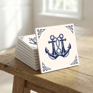 May include: A stack of square ceramic tiles with a navy blue anchor design. Each tile features a detailed anchor illustration with rope and decorative corner accents on a cream background. The tiles are arranged on a wooden surface.
