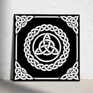 Può includere: Un quadrato nero con un disegno a nodo celtico bianco. Il disegno presenta un nodo triquetra centrale all'interno di un cerchio, circondato da un bordo intrecciato e accenti angolari. L'opera d'arte è esposta su una parete bianca.