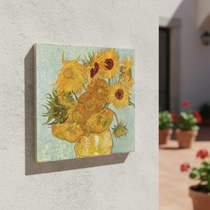 May include: Square canvas art depicting a still life of sunflowers in a yellow vase. The painting has a light blue background and is mounted on a wooden frame. The sunflowers are yellow and brown, with green leaves.