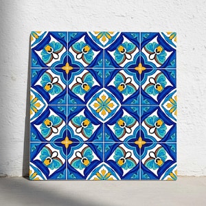 Puede incluir: Arreglo de baldosas cuadradas con un patrón repetitivo de diseños florales azules, amarillos y blancos. Las baldosas tienen un acabado brillante y están dispuestas en una cuadrícula, creando una superficie decorativa. La estética general recuerda a los azulejos mediterráneos tradicionales.