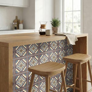 May include: A kitchen island with a wooden countertop and decorative tile paneling. The tiles feature a repeating pattern of blue, cream, and gold geometric designs. Two wooden stools are positioned in front of the island. A coffee maker, mug, and plant are on the countertop.