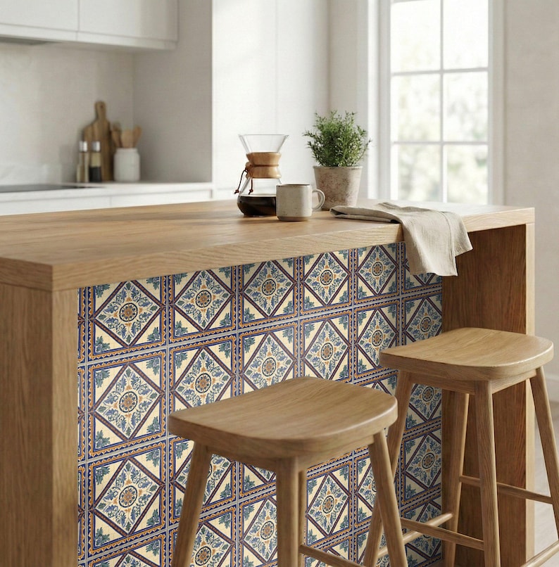 May include: A kitchen island with a wooden countertop and decorative tile paneling. The tiles feature a repeating pattern of blue, cream, and gold geometric designs. Two wooden stools are positioned in front of the island. A coffee maker, mug, and plant are on the countertop.