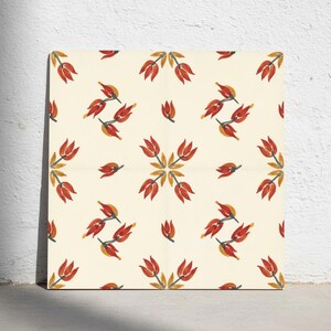 Op de afbeelding: Een vierkante tegel met een herhalend patroon van gestileerde, tulpachtige bloemen in rood en oranje op een crèmekleurige achtergrond. De bloemmotieven zijn gerangschikt in symmetrische clusters en individuele stengels.