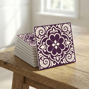 Può includere: Una pila di sottobicchieri quadrati in ceramica con un motivo floreale. I sottobicchieri hanno uno sfondo viola scuro con un motivo floreale color crema. I sottobicchieri sono impilati su una superficie di legno.