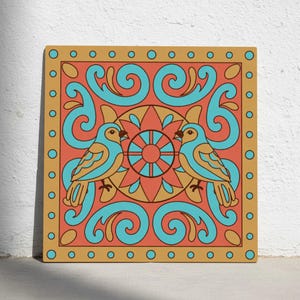 Puede incluir: Arte mural cuadrado con dos pájaros estilizados enfrentados, sobre un fondo coral con detalles turquesa y dorados. La obra tiene un borde dorado con pequeños detalles circulares, creando un diseño simétrico.