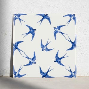 Puede incluir: Un azulejo cuadrado de cerámica con un patrón repetitivo de golondrinas azules en varias posiciones de vuelo sobre un fondo blanco sólido. Las aves están representadas en un estilo de tinta azul, mostrando plumas detalladas y colas largas.