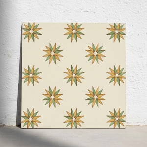Puede incluir: Un azulejo cuadrado con un patrón repetitivo de estrellas de doce puntas en tonos alternos de amarillo mostaza y verde salvia sobre un fondo color crema, con cada estrella centrada alrededor de un pequeño punto blanco.