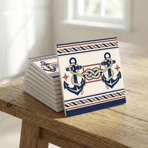 Op de afbeelding: Een stapel vierkante onderzetters met een nautisch thema. Elke onderzetter heeft een crèmekleurige achtergrond met marineblauwe ankers, touwen en rood-gouden randen. De onderzetters zijn gestapeld op een houten oppervlak.