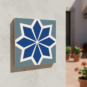 Puede incluir: Azulejo decorativo cuadrado con un diseño de estrella azul y blanco. El azulejo está montado en una pared blanca, mostrando un patrón geométrico con un fondo azul claro y una estrella central de ocho puntas.