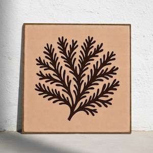 Puede incluir: Azulejo decorativo cuadrado con un diseño de árbol marrón oscuro sobre un fondo beige claro. El azulejo tiene un borde marrón y se muestra contra una pared blanca. La obra de arte es una ilustración botánica minimalista.