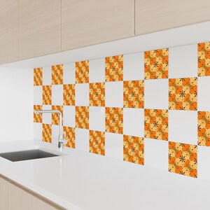 May include: A kitchen backsplash featuring a repeating pattern of orange, yellow, and green floral designs on white square tiles. The tiles are arranged in a checkerboard pattern above a white countertop and sink.