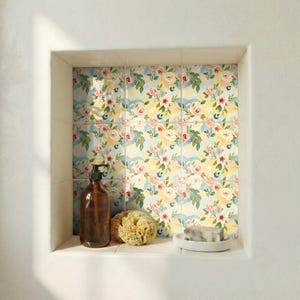 May include: A built-in bathroom shelf with floral patterned tiles. A brown soap dispenser, a natural sponge, and a bar of soap on a white dish are on the shelf. The tiles have a light blue, yellow, and pink floral design.