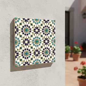 Puede incluir: Arte mural cuadrado con un patrón geométrico repetitivo en tonos azules, turquesas y dorados sobre un fondo blanco. El diseño recuerda a la azulejería marroquí. La obra de arte está montada en una pared blanca.