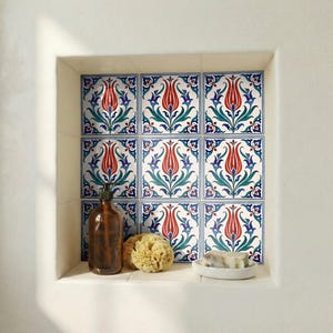 May include: A bathroom niche features decorative tiles with a red tulip design, accented by green leaves and blue borders. A brown bottle, a natural sponge, and a bar of soap on a white dish complete the scene.