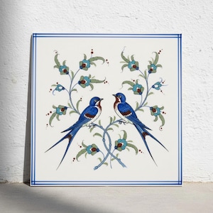 May include: A square ceramic tile featuring a white background with a blue double-line border. The design displays two blue birds with brown accents facing each other, surrounded by symmetrical green and blue floral vine patterns.