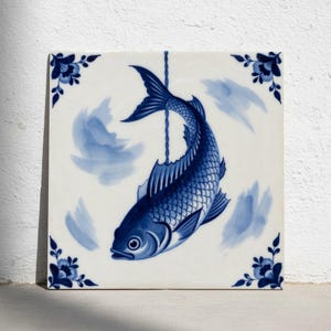 Könnte beinhalten: Quadratische Keramikfliese mit einem blau-weißen Fischdesign. Der Fisch hängt an einer Schnur vor einem weißen Hintergrund mit blauen Pinselstrichen. Florale Eckakzente verzieren die Fliese.