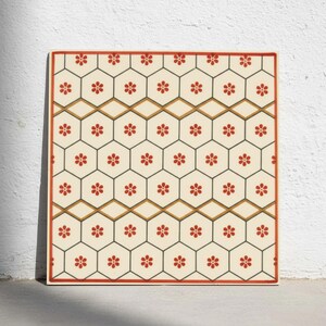 Può includere: Una piastrella quadrata con un motivo ripetitivo di esagoni color crema delineati in grigio scuro. Ogni esagono contiene un piccolo fiore rosso a sei petali. Bande orizzontali di rombi dorati attraversano la griglia, incorniciate da un bordo rosso.
