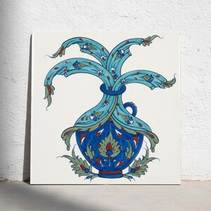 May include: A square ceramic tile featuring a hand-painted illustration of a blue vase with a narrow neck and a rounded body. The vase is adorned with intricate floral motifs in shades of turquoise, dark blue, red, and sage green.