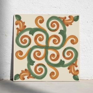 Puede incluir: Un azulejo de cerámica cuadrado con fondo color crema y un patrón simétrico pintado a mano de volutas verdes y naranjas entrelazadas. El diseño irradia desde el centro, con detalles de hojas en cada esquina del azulejo.