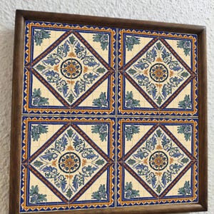 May include: A framed set of four decorative ceramic tiles. Each tile features a cream-colored background with a blue, yellow, and green floral design. The tiles are framed in a dark brown wooden frame, creating a cohesive decorative piece.