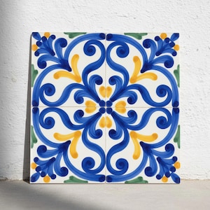 Pode incluir: Um azulejo decorativo quadrado com um padrão simétrico de volutas azuis, detalhes amarelos em forma de pétalas e pequenos motivos de folhas verdes sobre um fundo branco. O design é composto por quatro azulejos menores juntos.