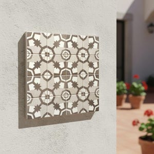 Puede incluir: Un conjunto de baldosas decorativas cuadradas con un patrón geométrico de estrellas y hexágonos en tonos grises, beige y blanco. Las baldosas están montadas en una pared blanca, mostrando un diseño moderno para la decoración del hogar.