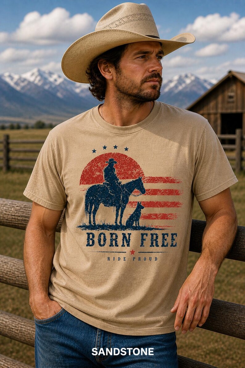 Op de afbeelding: T-shirt in zandkleur met een afbeelding van een cowboy te paard, een hond en de tekst "BORN FREE" en "RIDE PROUD". Het ontwerp bevat rode en blauwe elementen. Het woord "SANDSTONE" staat onderaan.