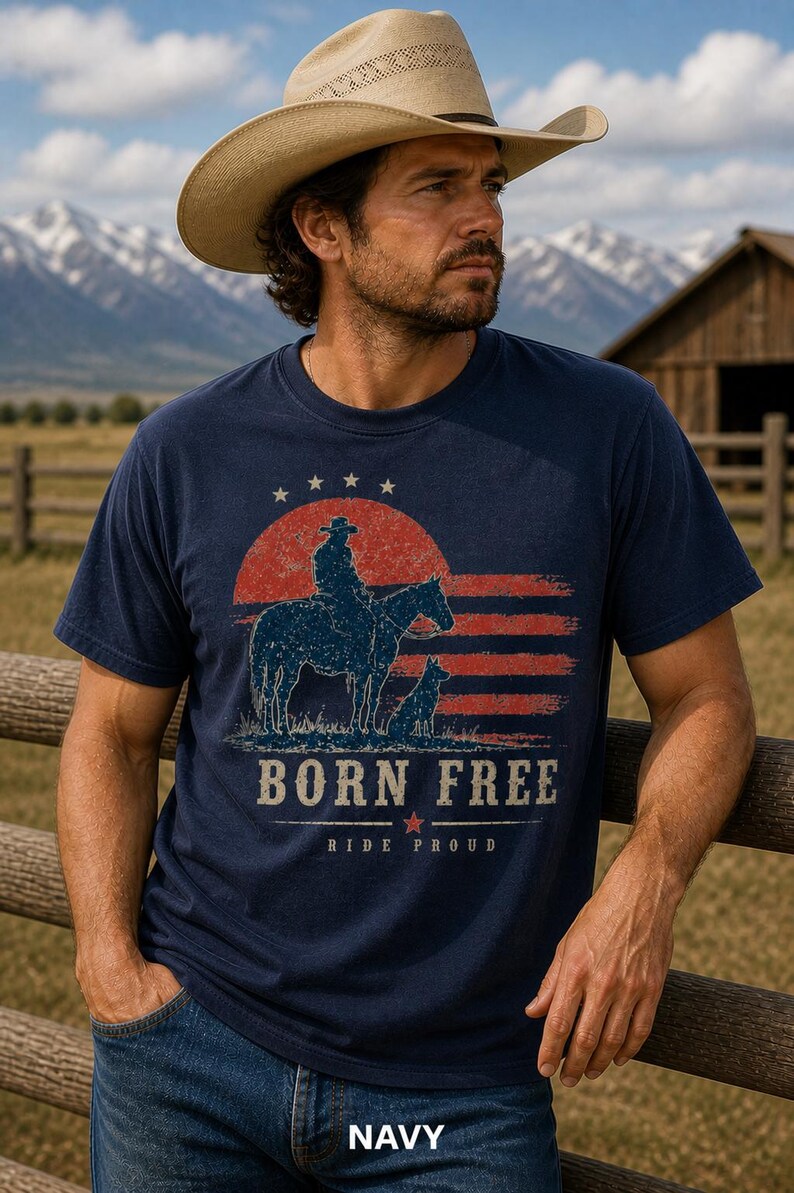 Op de afbeelding: Marineblauw T-shirt met een afbeelding van een cowboy op een paard, een hond en de tekst "BORN FREE RIDE PROUD". Het ontwerp bevat een rood-witte gestreepte achtergrond en een rode zon. Het woord "NAVY" staat onderaan.