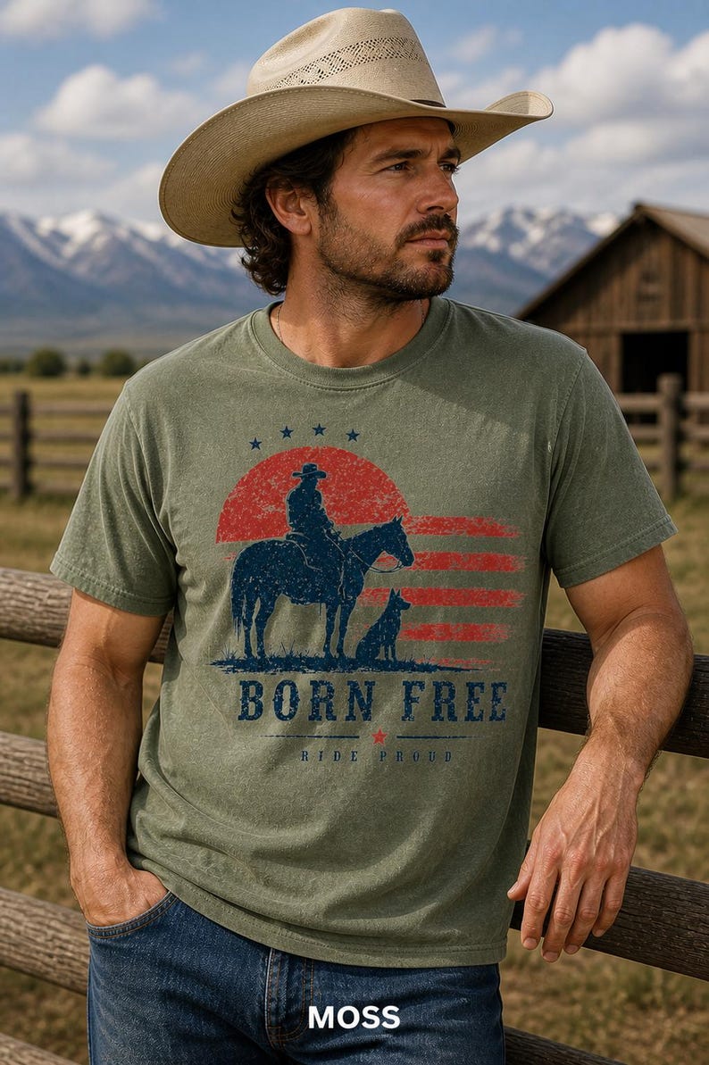 Op de afbeelding: Mosgroen t-shirt met een afbeelding van een cowboy te paard, een hond en de tekst "BORN FREE". Het ontwerp bevat een rode en blauwe zonsondergang en sterren. Het model draagt een cowboyhoed en een blauwe spijkerbroek.