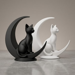 Peut inclure: Deux figurines de chat, une noire mate et une blanche mate, chacune assise sur une base en forme de croissant de lune. Les chats sont positionnés de profil, tournés vers l'avant avec des surfaces lisses et des bases arrondies stables.