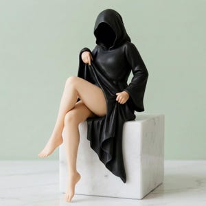 Puede incluir: Estatua de una figura negra con capucha sentada sobre un cubo de mármol blanco. La cara de la figura está oscurecida por la capucha, y la túnica se levanta para revelar las piernas. La estatua está sobre un fondo verde pálido.
