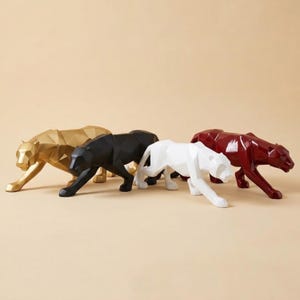 Peut inclure: Quatre sculptures géométriques de panthères en or, noir, blanc et bordeaux. Chaque panthère est en position de chasse, avec une patte avant tendue. Les sculptures ont un design à facettes, leur donnant un aspect moderne. Le fond est de couleur beige uni.