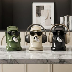 Peut inclure: Trois boîtes à mouchoirs en céramique en forme de tête Moai, vertes, crème et noires. Chacune porte des lunettes de soleil noires et un mouchoir sortant de la bouche. Les modèles crème et noirs ont des écouteurs.