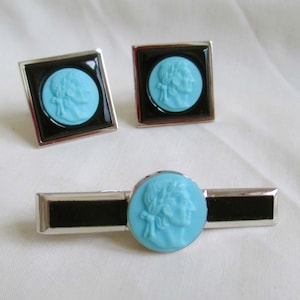 Op de afbeelding: Een set vintage manchetknopen en een stropdasclip. De manchetknopen zijn vierkant met een zwarte rand en een lichtblauwe camee. De stropdasclip heeft een vergelijkbaar ontwerp. De set is zilverkleurig.