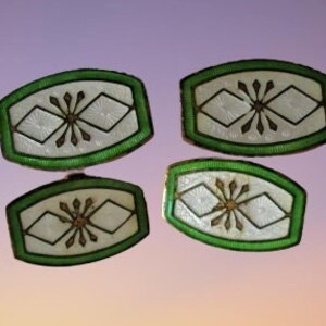 May include: Four vintage cufflinks with a green border, white center, and a gold-colored starburst design. The cufflinks have a rectangular shape with rounded edges. The background is a gradient of purple and orange.