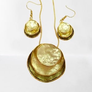 May include: A gold-coloured jewellery set comprising a necklace and earrings. The necklace features a pendant with three overlapping, textured, circular elements. The earrings echo the pendant's design. The set is displayed against a white backdrop.