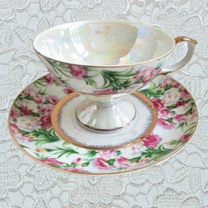 May include: A white teacup and saucer with a floral pattern. The cup has a gold rim and a delicate handle. The saucer has a matching floral pattern and a gold trim.