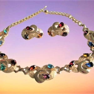 May include: A gold tone necklace and earrings set with a multi-coloured rhinestone design. The necklace features a chain link design and the earrings are clip-on.