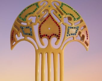 May include: A yellow plastic hair comb with a decorative design featuring a geometric pattern with red, green, and blue rhinestones.